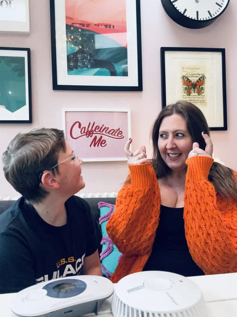 Woman in orange cardigan smiles, discussing smoke alarms for deaf people with a boy in spectacles.