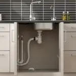 Kitchen sink cupboard open to show pipes and FA7011-EUX4 under the sink.