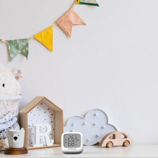 Nursery shelf with toys, an FA7312-EUX4 digital thermometer, and a colourful pennant bunting.