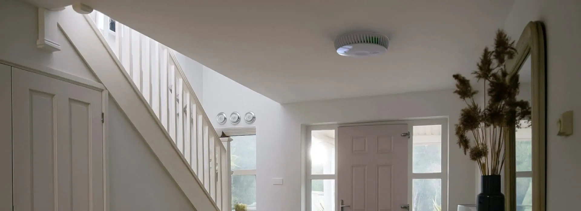 Bright hallway with staircase, mirror, and a round air purifier for CO hazards on the ceiling.