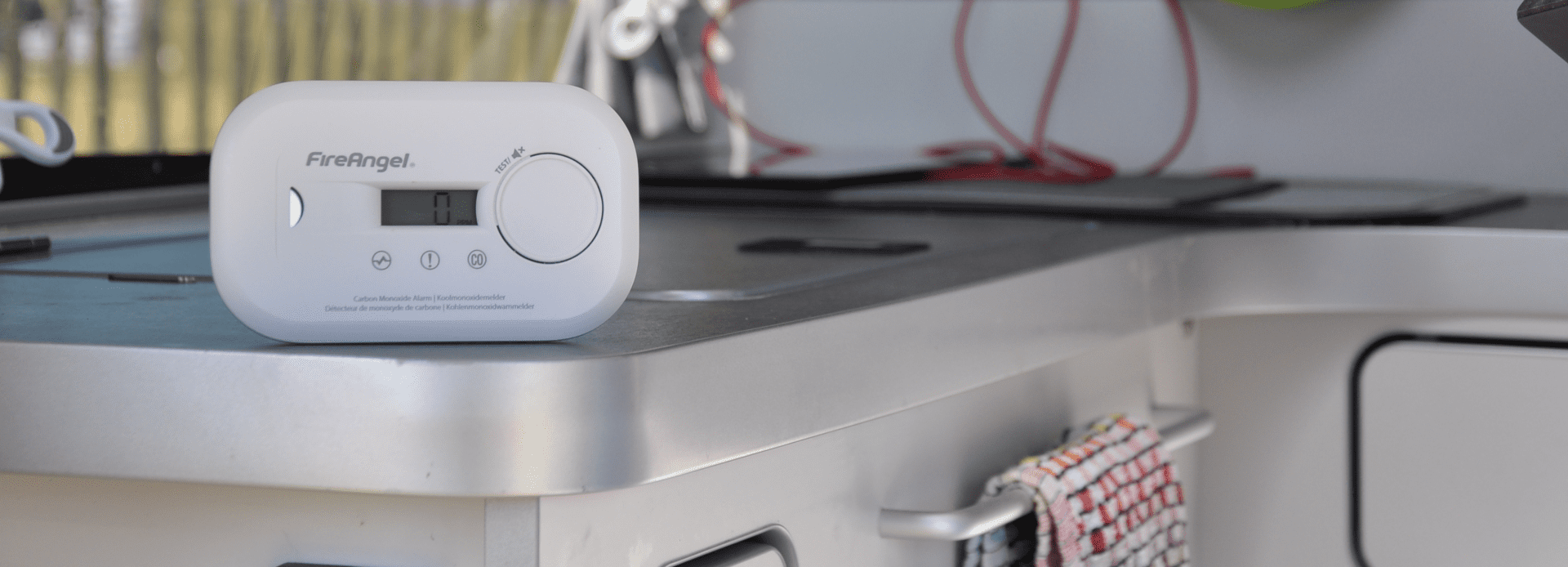 White carbon monoxide alarm on a kitchen worktop promotes campervan safety near the cooker.