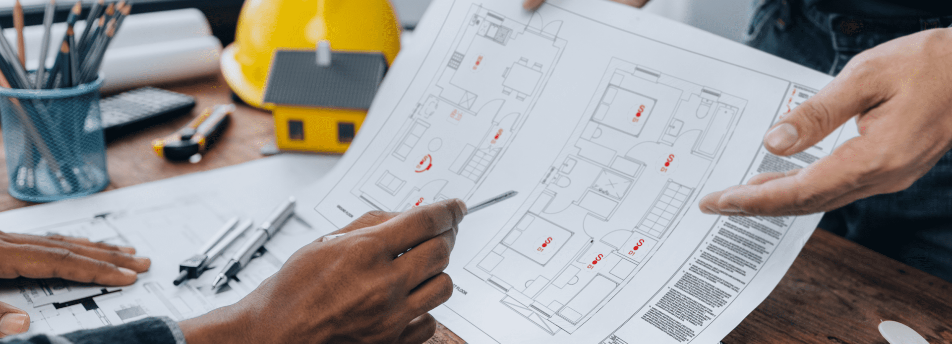 Two people review a house floor plan, focusing on fire safety design with tools and a model house.