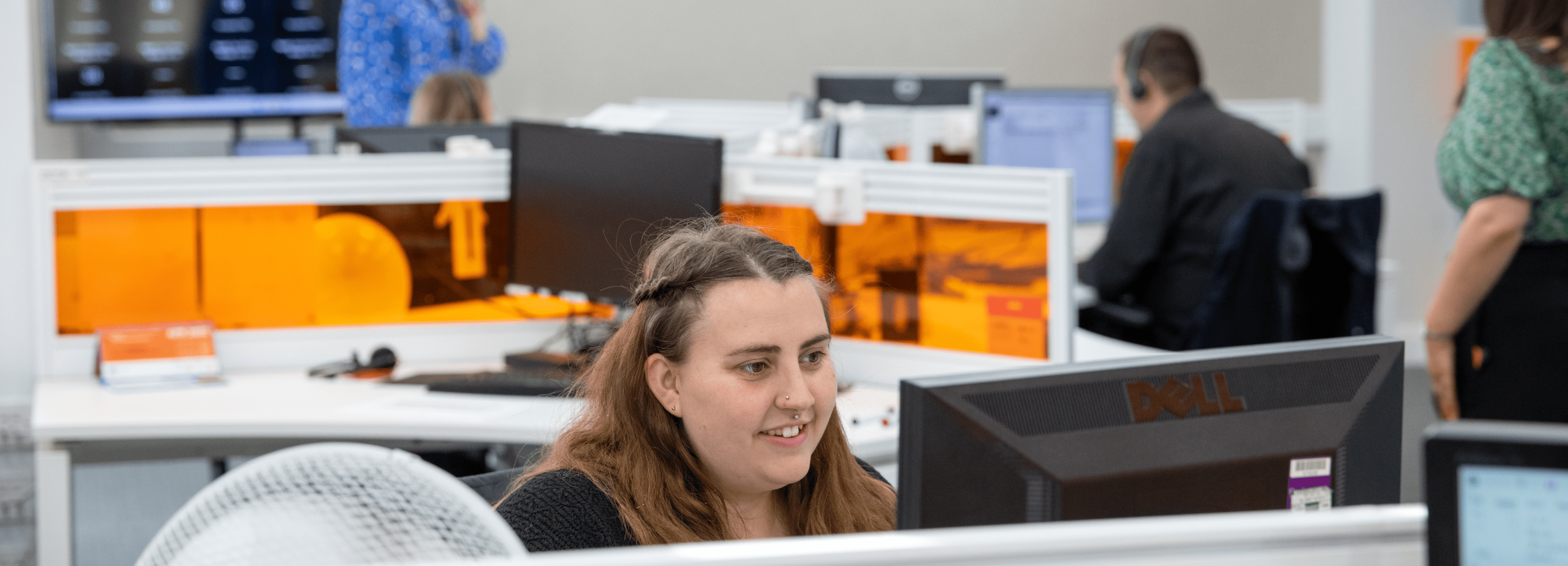 Woman providing Customer Support at a computer in a busy open-plan office.