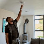 Man tests a Spec+ Multi-Sensor Smoke, Heat & CO Alarm on the ceiling of a modern living room.