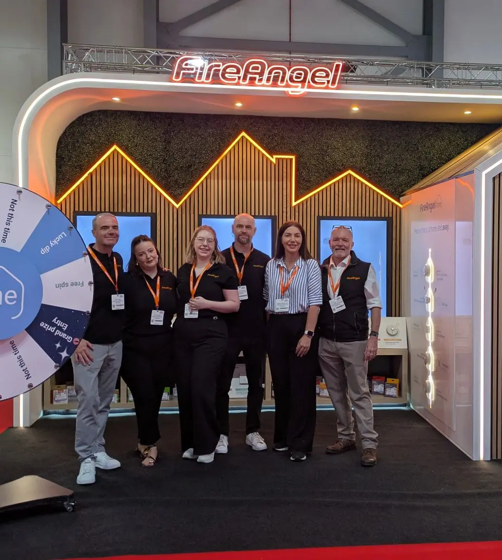Six people pose before a FireAngel One trade show stand with a prize wheel.