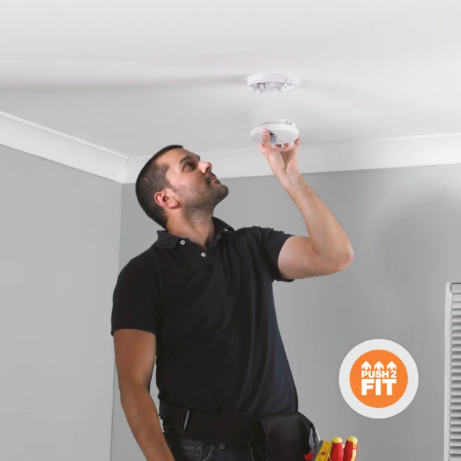 A man installs a smoke alarm on a white ceiling in a modern room.